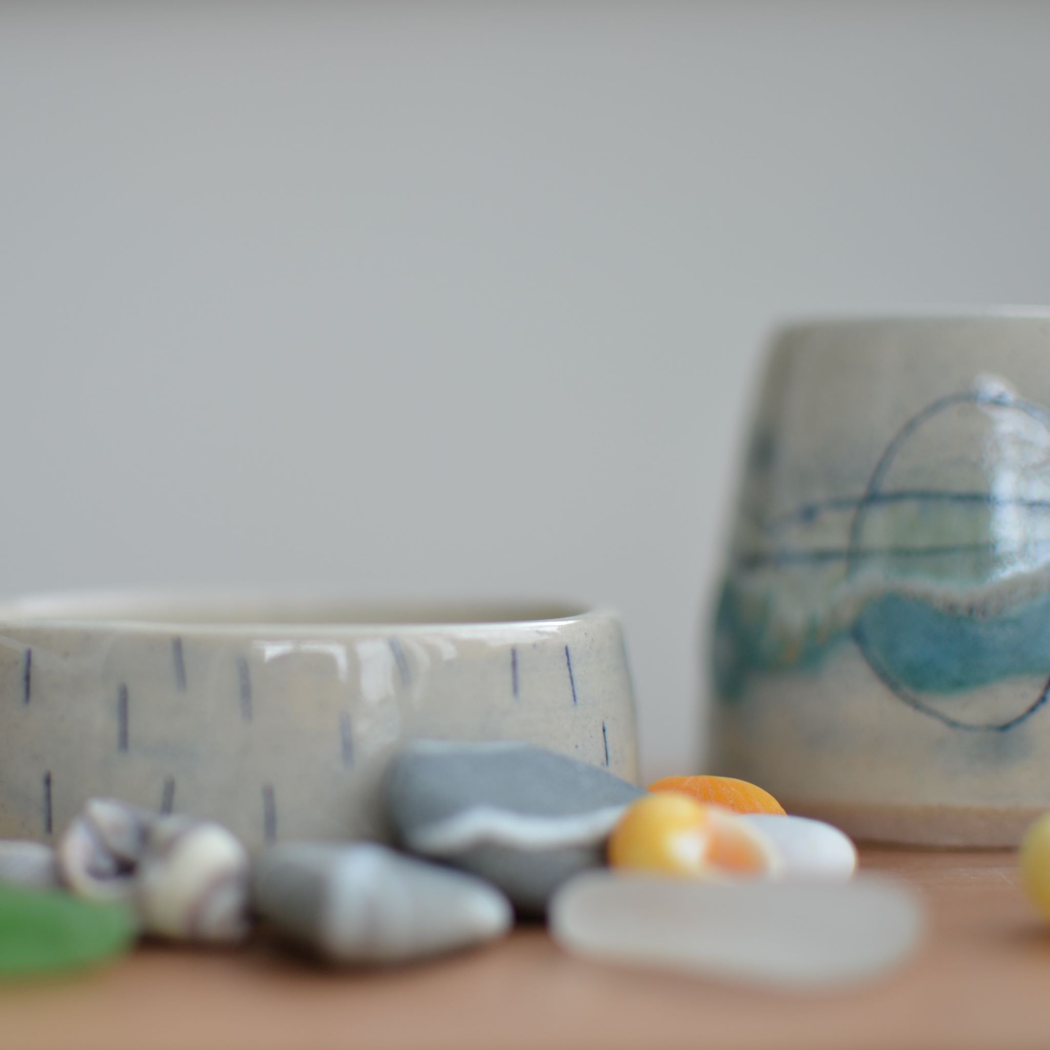 A dip bowl and small jug glazed in delicate sea colours surrounded with seashore stones and shells