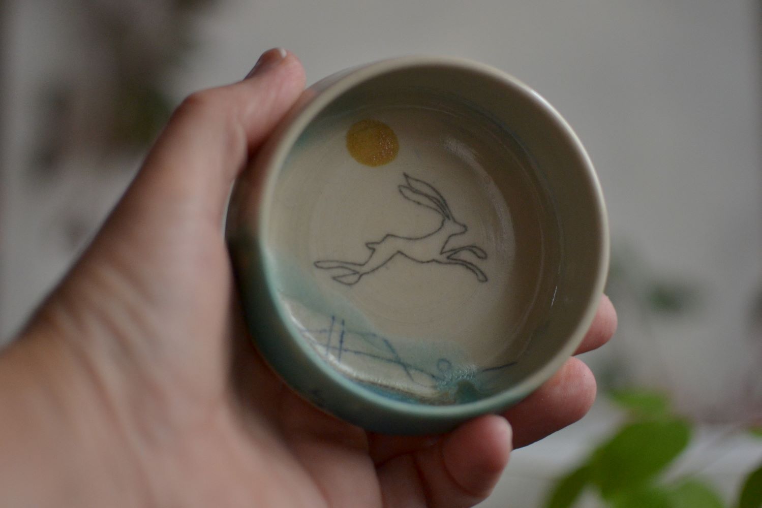 A hand holding a handmade ceramics dish with an image of a hare running across it.